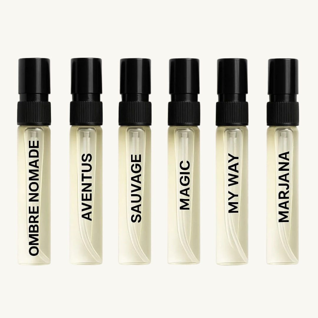 Six clear Senti perfume sample vials with black caps, labeled Ombre Nomade, Aventus, Sauvage, Magic, My Way, and Marjana, displayed in a row on a light background.